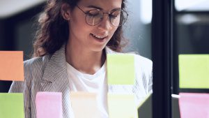 Foto de mulher em frente a uma parede de vidro cheia de post-its.